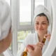 Une femme en serviette se regarde dans le miroir, réfléchissant à son apparence.