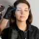 Une esthéticienne professionnelle utilise une pince à épiler pour préparer les sourcils d'une cliente avant une procédure de maquillage permanent.