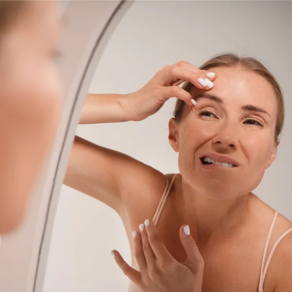 A woman gazes into a mirror, her hands gently resting on her face, reflecting a moment of contemplation.