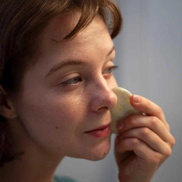 A woman holds a piece of paper to her face, partially obscuring her features while looking contemplative.
