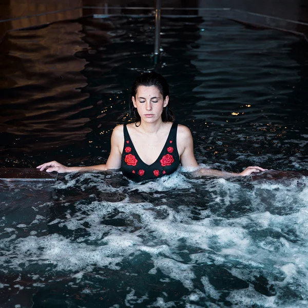 A woman in a black swimsuit relaxes in a thermal spa pool, surrounded by tranquil water.