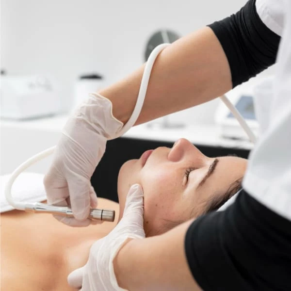 Une femme reçoit un soin du visage dans un salon de beauté, détendue sur une table de traitement.