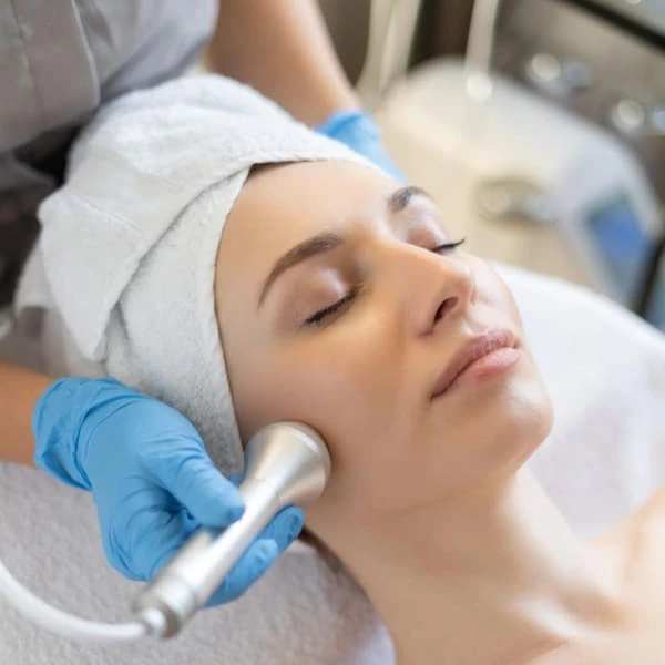 Une femme reçoit un soin du visage dans un salon de beauté, détendue sur une table de traitement.